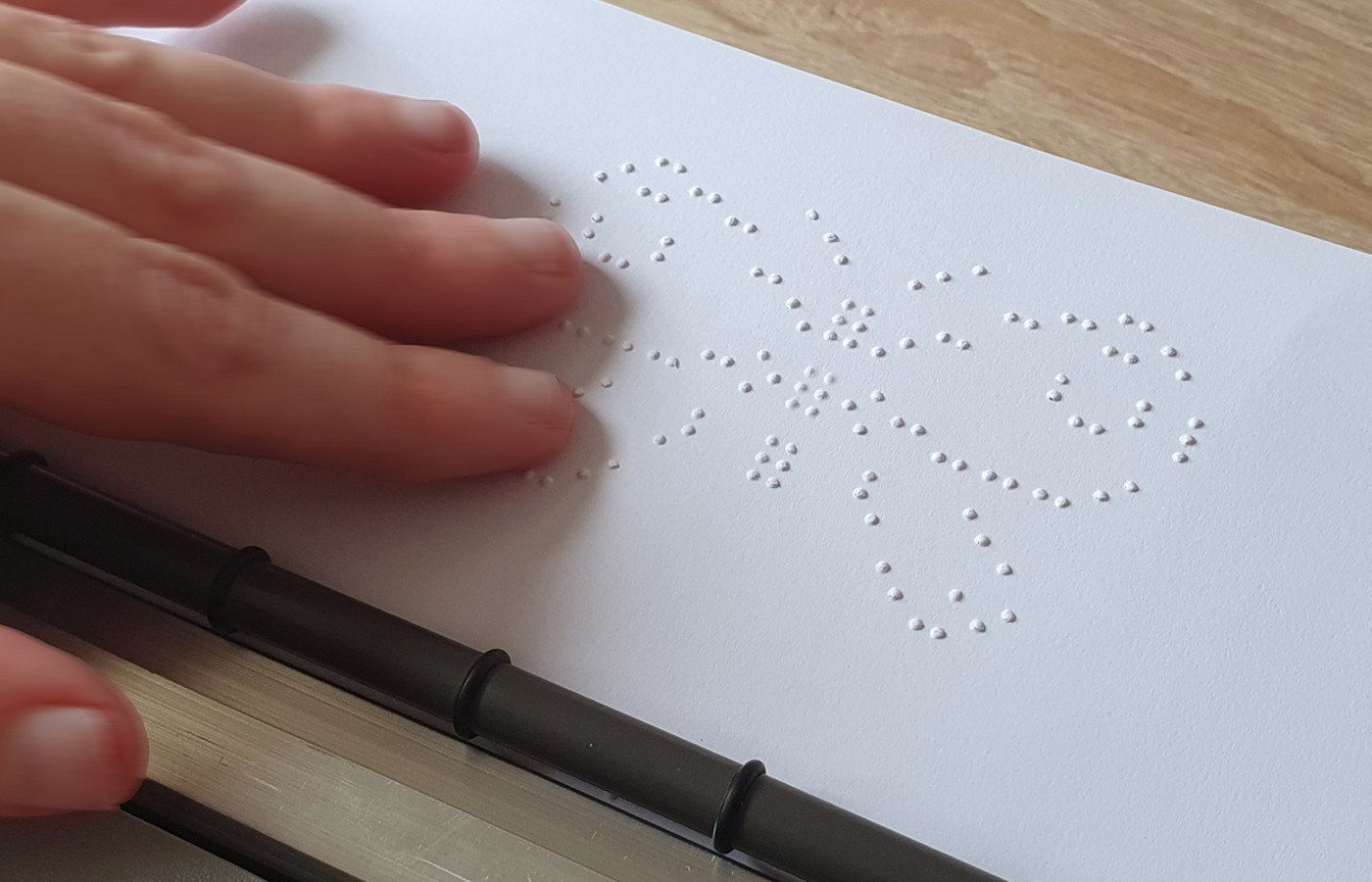 A hand touching the braille drawing of a butterfly on a sheet of paper